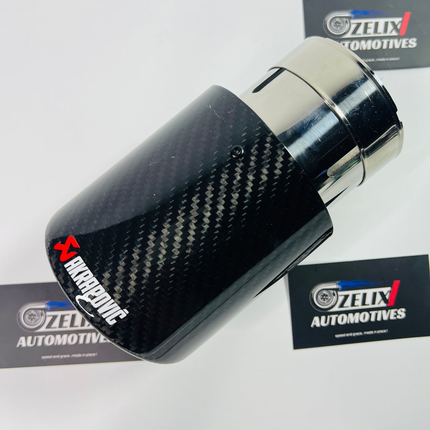 Gloss carbon round single exhaust tip shown from the front, with stainless-steel inlet visible