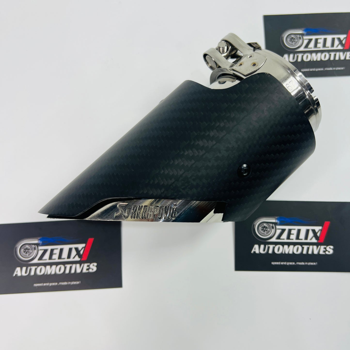 Matte carbon slant-cut exhaust tip shown from the front, highlighting the angled outlet and stainless steel clamp
